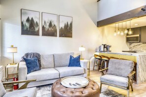 A modern living room with a grey sofa, two armchairs, a coffee table, and a kitchen area with a marble countertop. - Modern Tahoe Retreat - Your Place to Unwind (South Lake Tahoe)