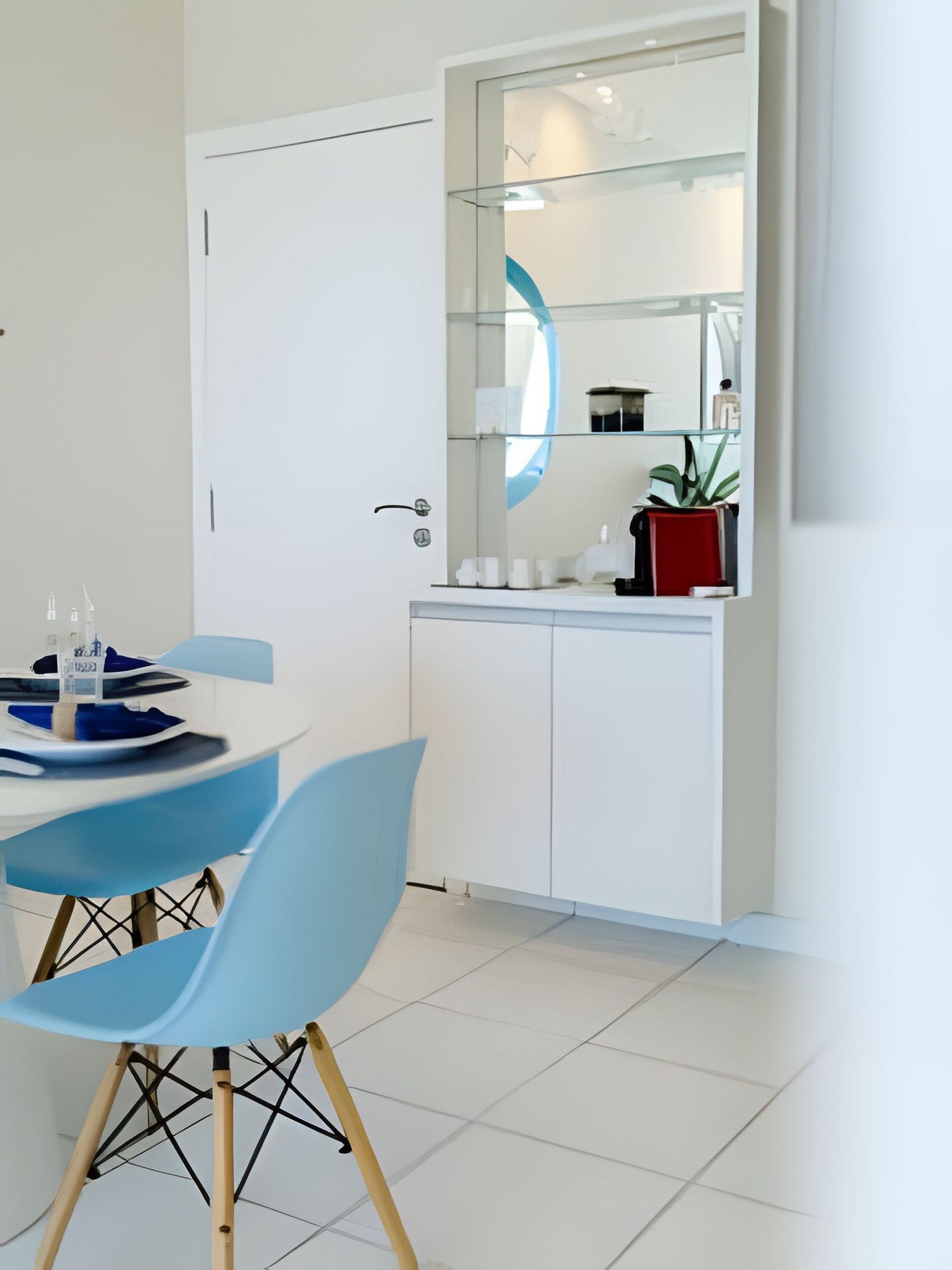 A modern kitchen with white cabinets, a glass backsplash, and a dining area with blue chairs.