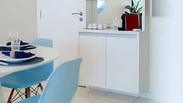 A modern kitchen with white cabinets, a glass backsplash, and a dining area with blue chairs.