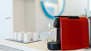 Un baño moderno con un estante de vidrio que contiene artículos de tocador, una cafetera roja y un lavamanos blanco.