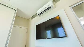 Una habitación con un televisor de pantalla plana montado, una puerta blanca y un equipo de aire acondicionado en el techo.