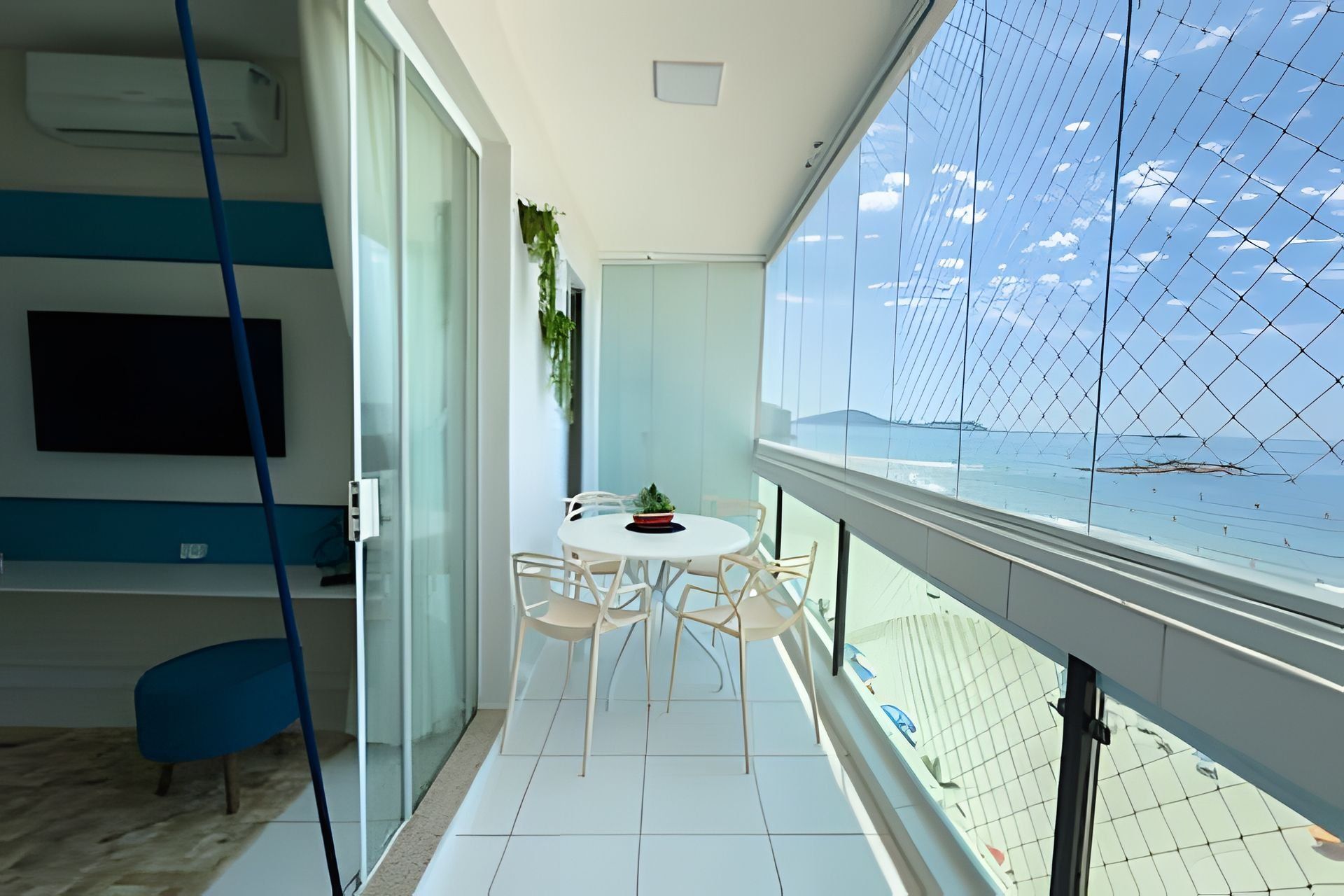 Una habitación moderna con balcón, una mesa redonda con sillas, una planta en maceta y un televisor fijado a la pared.