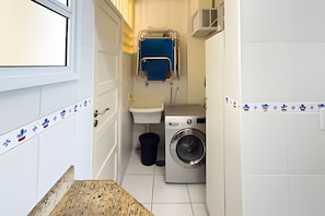 A compact laundry room with a washing machine, a sink, and a towel rack. - SHB - Desperte com o Azul do Mar (Guarujá)