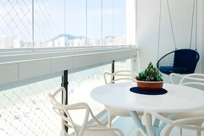 A modern room with a round white table, white chairs, a hanging chair, and a potted plant.