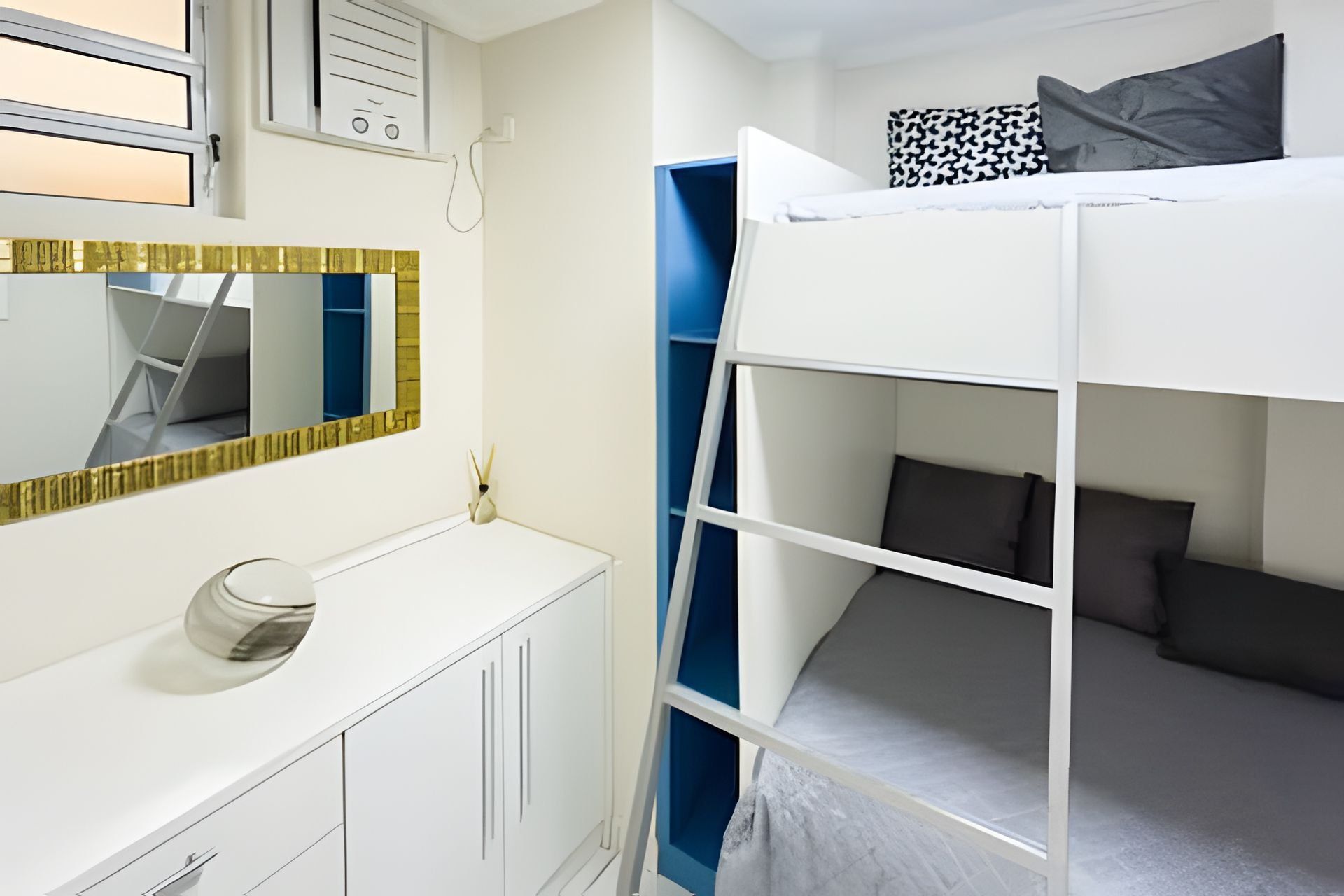 Quarto com beliche, toucador branco, espelho e uma pequena janela.