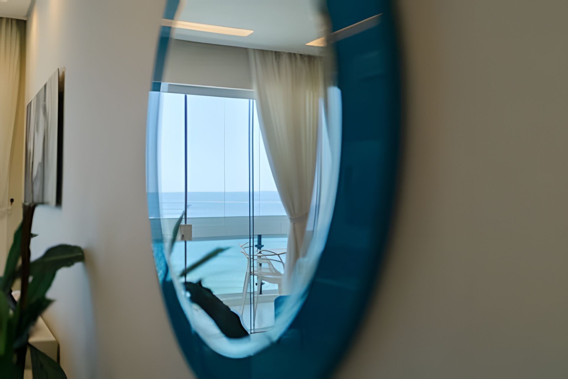 Una habitación con vista al océano a través de una ventana, una silla y una planta.