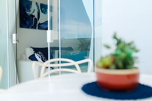 Una habitación moderna con una mesa blanca, una planta roja y vista a un barco a través de un muro de cristal.