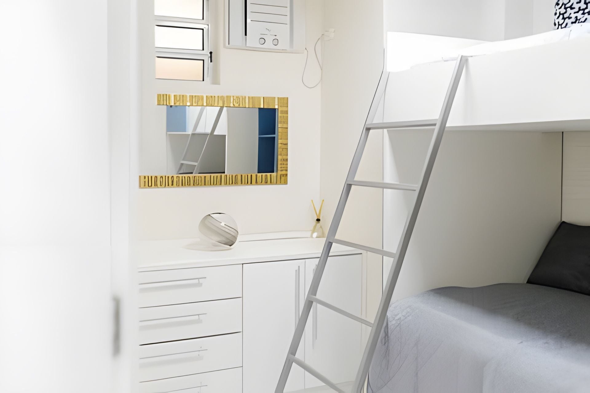 A bunk bed with a ladder, a white dresser with drawers, a mirror, and a window with blinds.