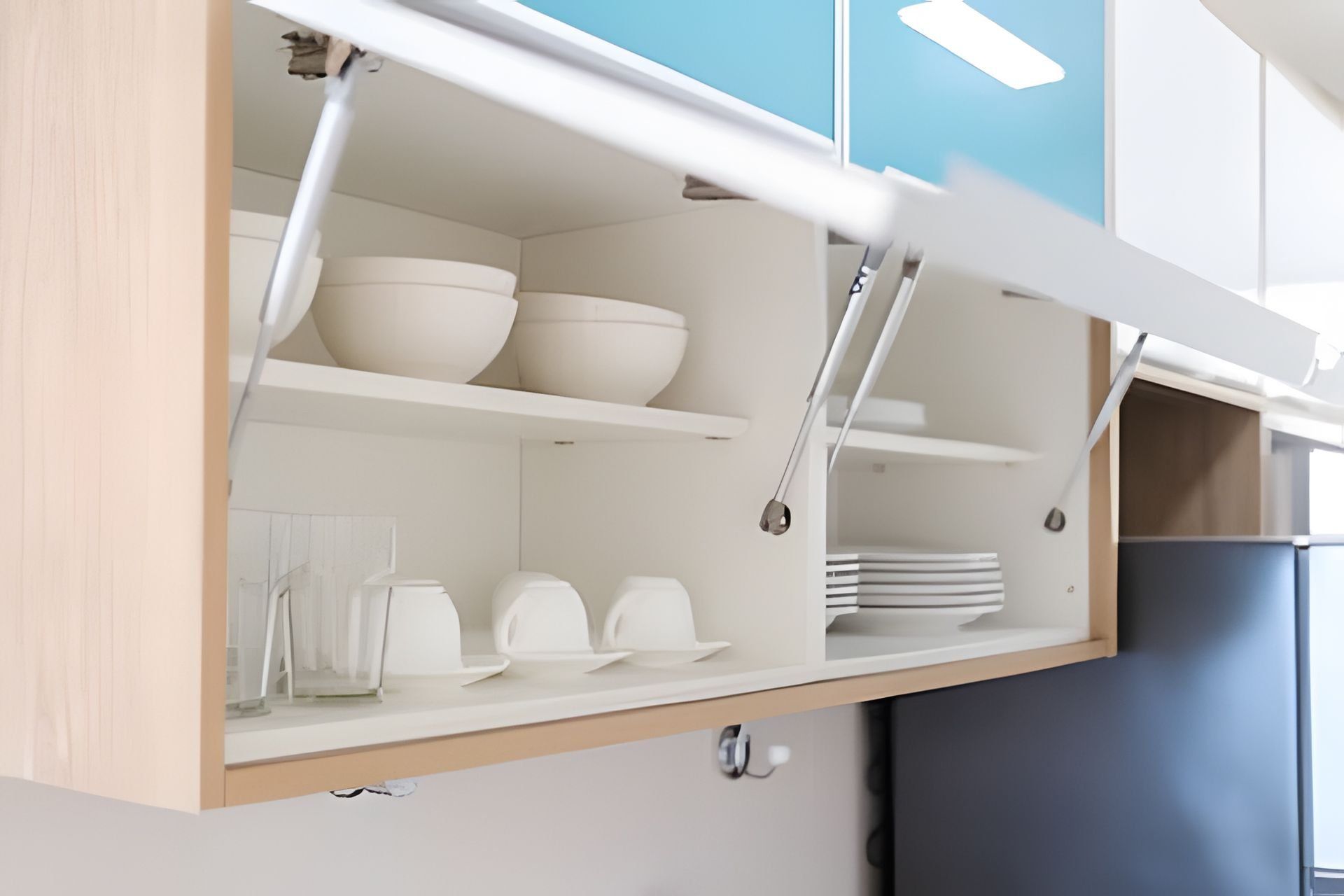 Una cocina con armarios blancos, un refrigerador azul y una repisa con cuencos y platos.