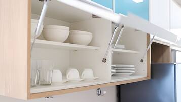 Una cocina con armarios blancos, un refrigerador azul y una repisa con cuencos y platos.