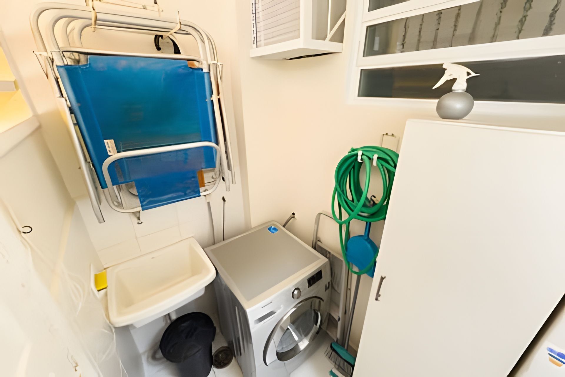Une petite pièce équipée d’un lave-linge, d’un petit évier et d’une fenêtre donnant sur un paysage agréable.