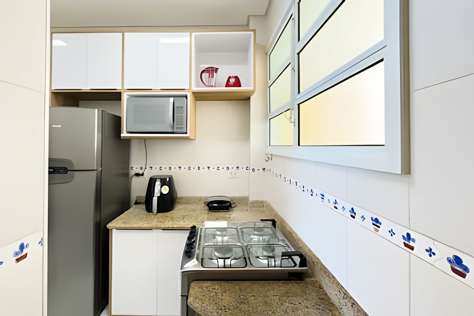 Una cocina compacta con armarios blancos, microondas, cafetera y estufa a gas.
