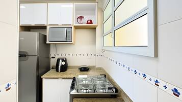 Una cocina compacta con armarios blancos, microondas, cafetera y estufa a gas.