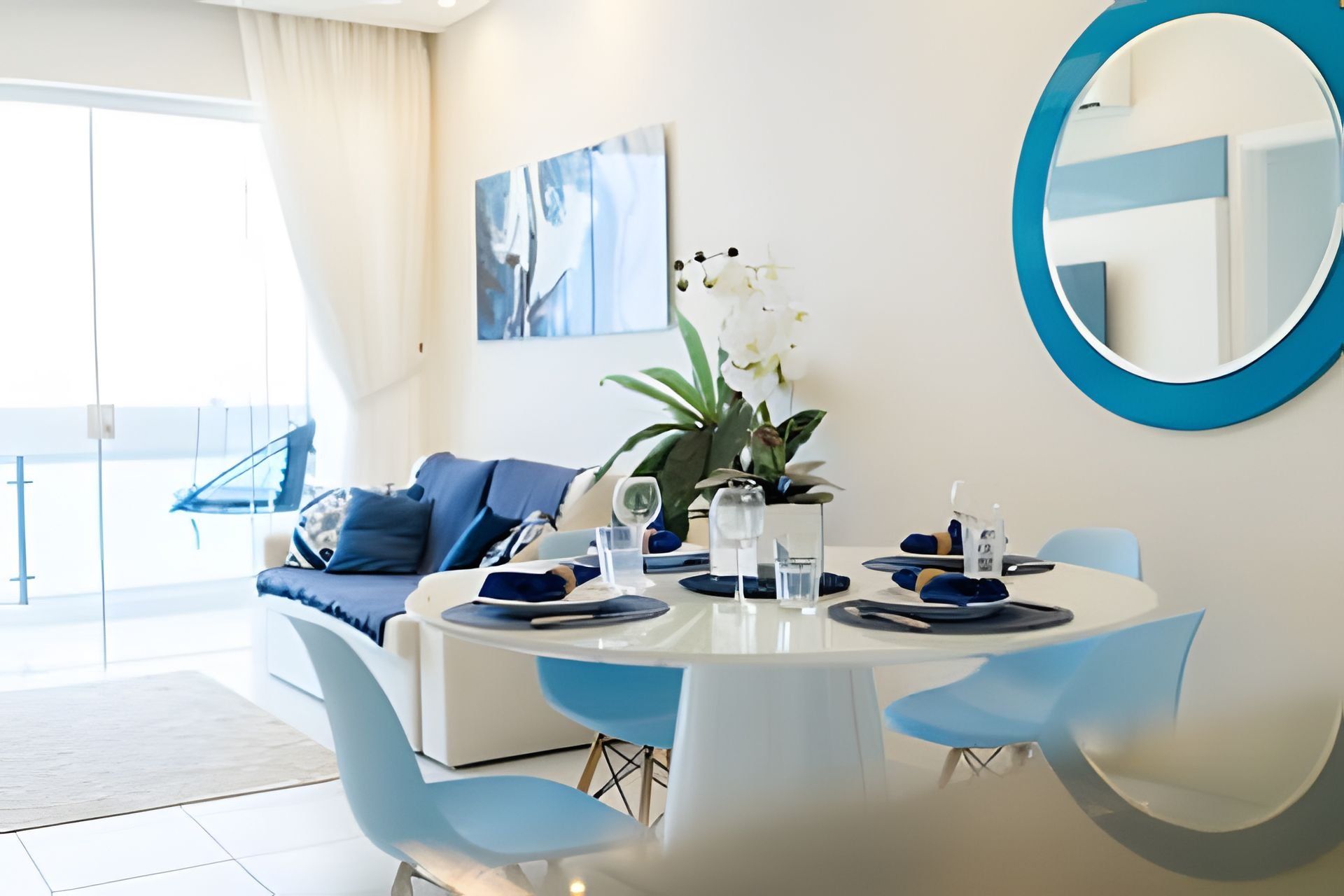 Un comedor moderno con una mesa redonda, sillas azules y un espejo grande en la pared.