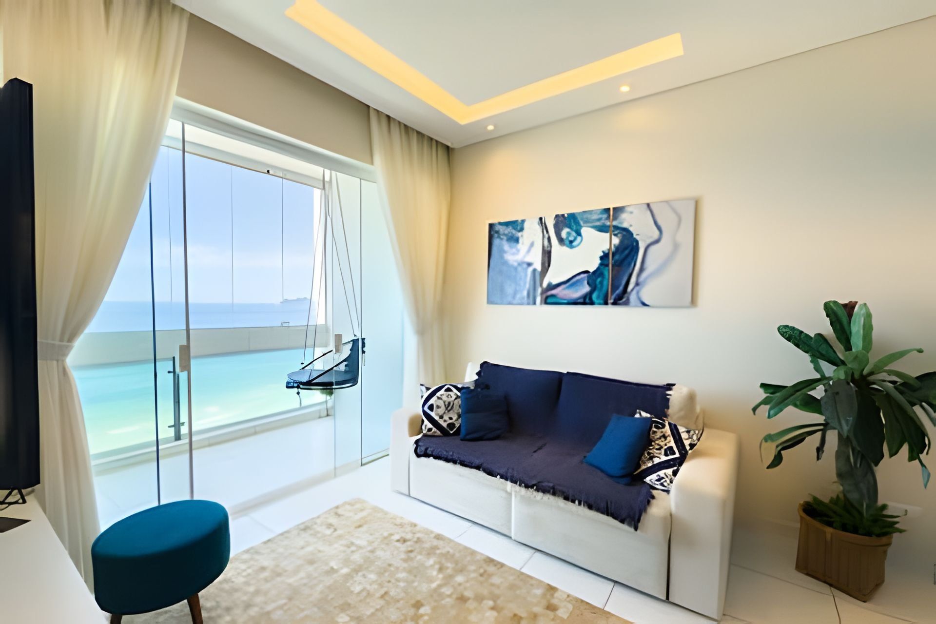Uma sala de estar moderna com um sofá, uma poltrona, uma janela grande com vista para o mar e um quadro na parede.