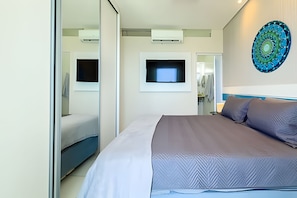 A modern hotel room with a large bed, a flat-screen TV mounted on the wall, and a decorative mirror. - SHB - Desperte com o Azul do Mar (Guarujá)