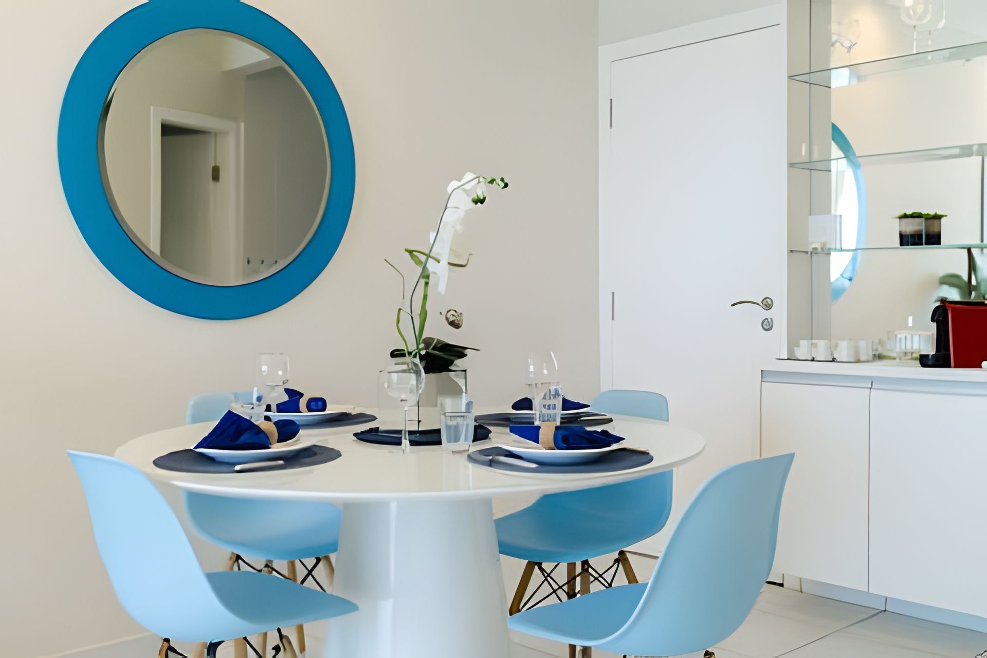 Un comedor con una mesa redonda, sillas azules y un espejo grande en la pared.