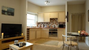 A compact kitchen with a dining area, a television, and a painting on the wall. - The Potions Room - A Magical Hot Tub Hideaway (Alnwick)