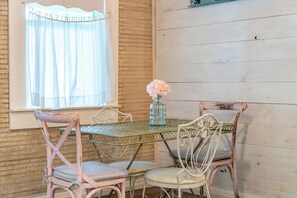A rustic dining area with a table and chairs, a window with sheer curtains, and a vase with flowers. - Telegraph Station #2,  Downtown, Pet friendly! (New Braunfels)