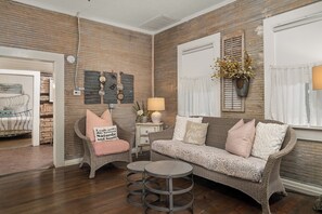A cozy living room with a wicker sofa, a small round table, and a chair with a cushion. - Telegraph Station #2,  Downtown, Pet friendly! (New Braunfels)
