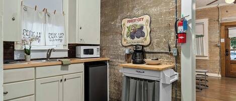 A kitchen with white cabinets, a microwave, a coffee machine, and a sign for Forest City brand blackberries.