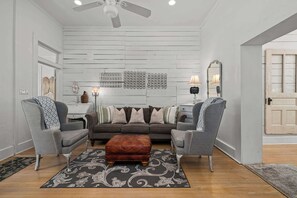 A living room with a grey sofa set, a brown ottoman, and a ceiling fan. - Historic Ludwig Haus, Downtown, Pet Friendly! (New Braunfels)