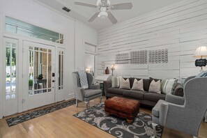 Ein Wohnzimmer mit grauem Sofa, grauem Sessel, braunem Hocker und einem gemusterten Teppich.