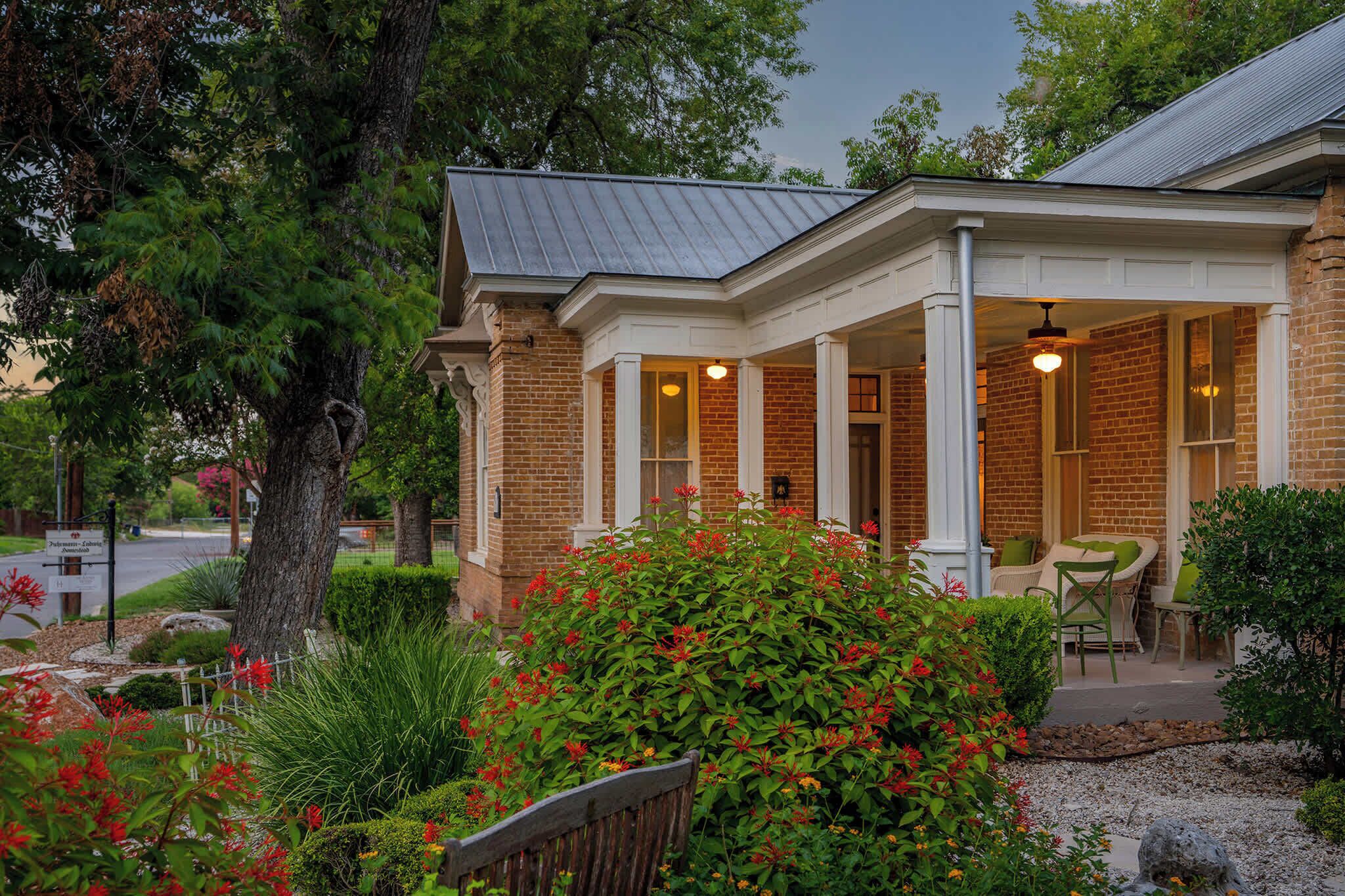 A brick building with a covered porch, outdoor seating, and a well-maintained garden.