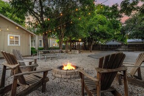 A patio area with wooden chairs, a fire pit, and string lights. - Historic Ludwig Haus, Downtown, Pet Friendly! (New Braunfels)