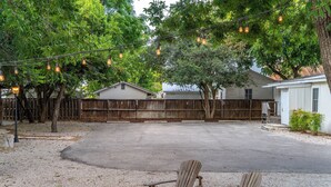 A backyard with a wooden fence, two Adirondack chairs, and string lights. - Telegraph Station #1, Downtown, Pet friendly! (New Braunfels)