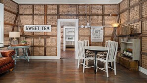 A room with a brick wall, a sign reading 'SWEET TEA', a dining table with chairs, a lamp, and a leather sofa. - Telegraph Station #1, Downtown, Pet friendly! (New Braunfels)