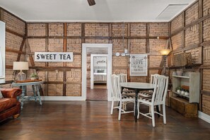 Ein Zimmer mit Ziegelwand, einem Schild mit der Aufschrift 'SWEET TEA', einem Esstisch mit Stühlen, einer Lampe und einem Ledersofa.