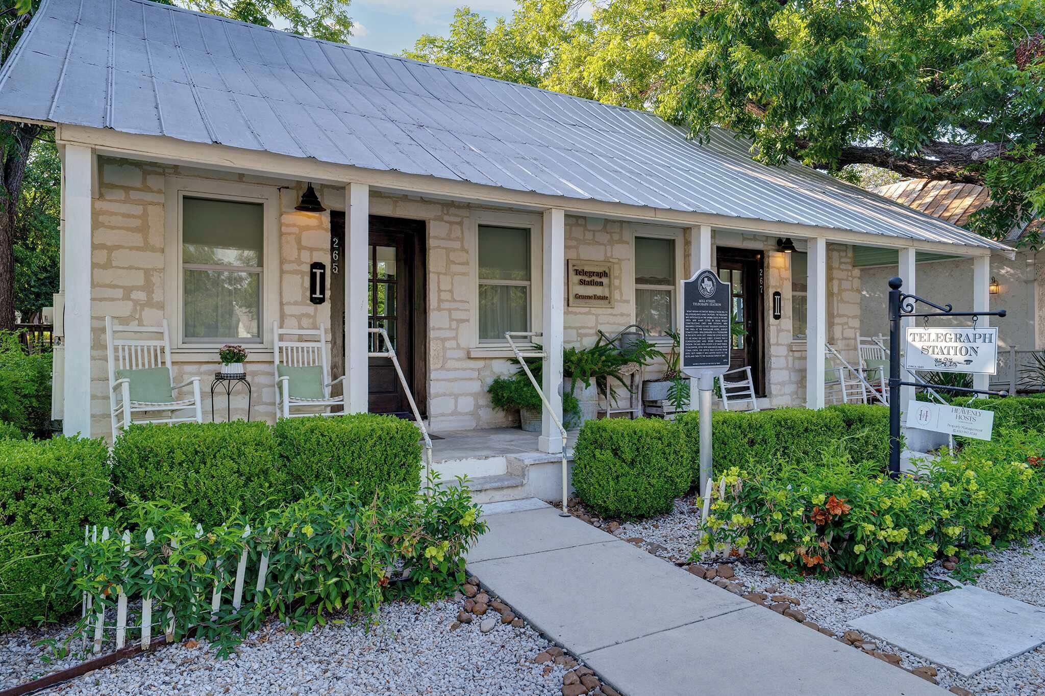 A stone building with a metal roof, a porch with two chairs, and a sign indicating it is a telegraph station.