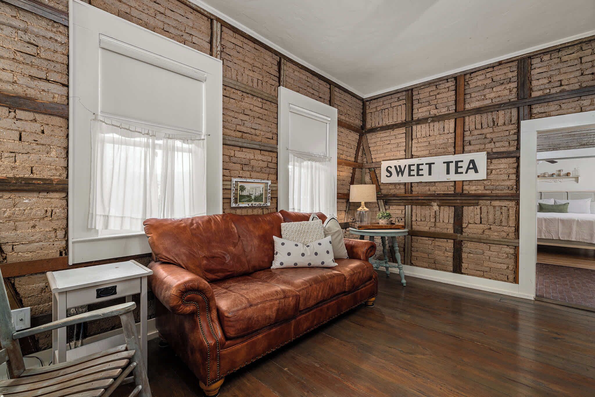 A room with a brown leather sofa, a small round table with a lamp, and a sign that reads 'SWEET TEA'.