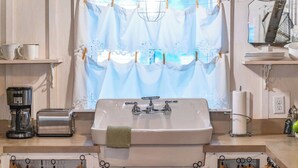 A kitchen with a sink, coffee maker, toaster, and a window with curtains. - Carriage Haus, Downtown, Pet Friendly! (New Braunfels)