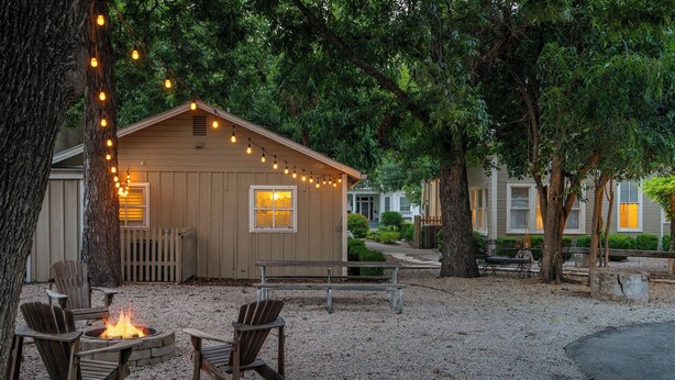 A wooden cabin with string lights, a fire pit, and Adirondack chairs. - Carriage Haus, Downtown, Pet Friendly! (New Braunfels)