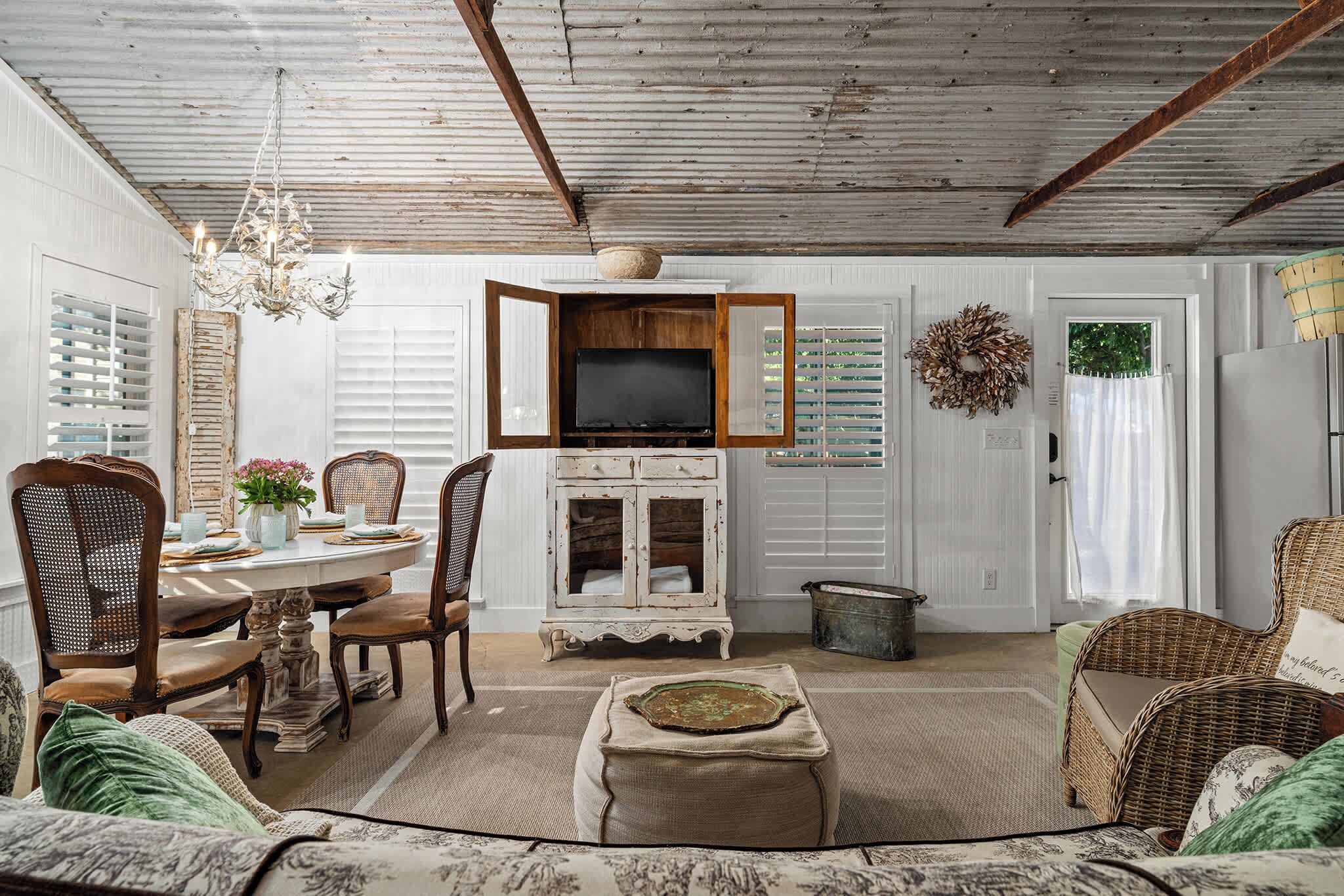 A rustic interior with a dining area, a television mounted on a wooden cabinet, and a wicker sofa.