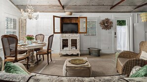 A rustic interior with a dining area, a television mounted on a wooden cabinet, and a wicker sofa. - Carriage Haus, Downtown, Pet Friendly! (New Braunfels)