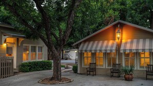 A two-story building with a porch, a tree in the center, and a small shed with a striped awning. - Carriage Haus, Downtown, Pet Friendly! (New Braunfels)