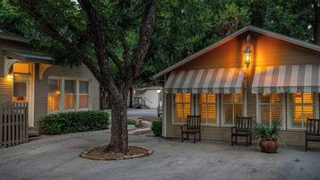 A two-story building with a porch, a tree in the center, and a small shed with a striped awning.
