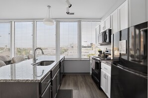 A modern kitchen with a large island, stainless steel appliances, and a view of the city through large windows. - Downtown Condo | Walk to Playhouse Square (Cleveland)