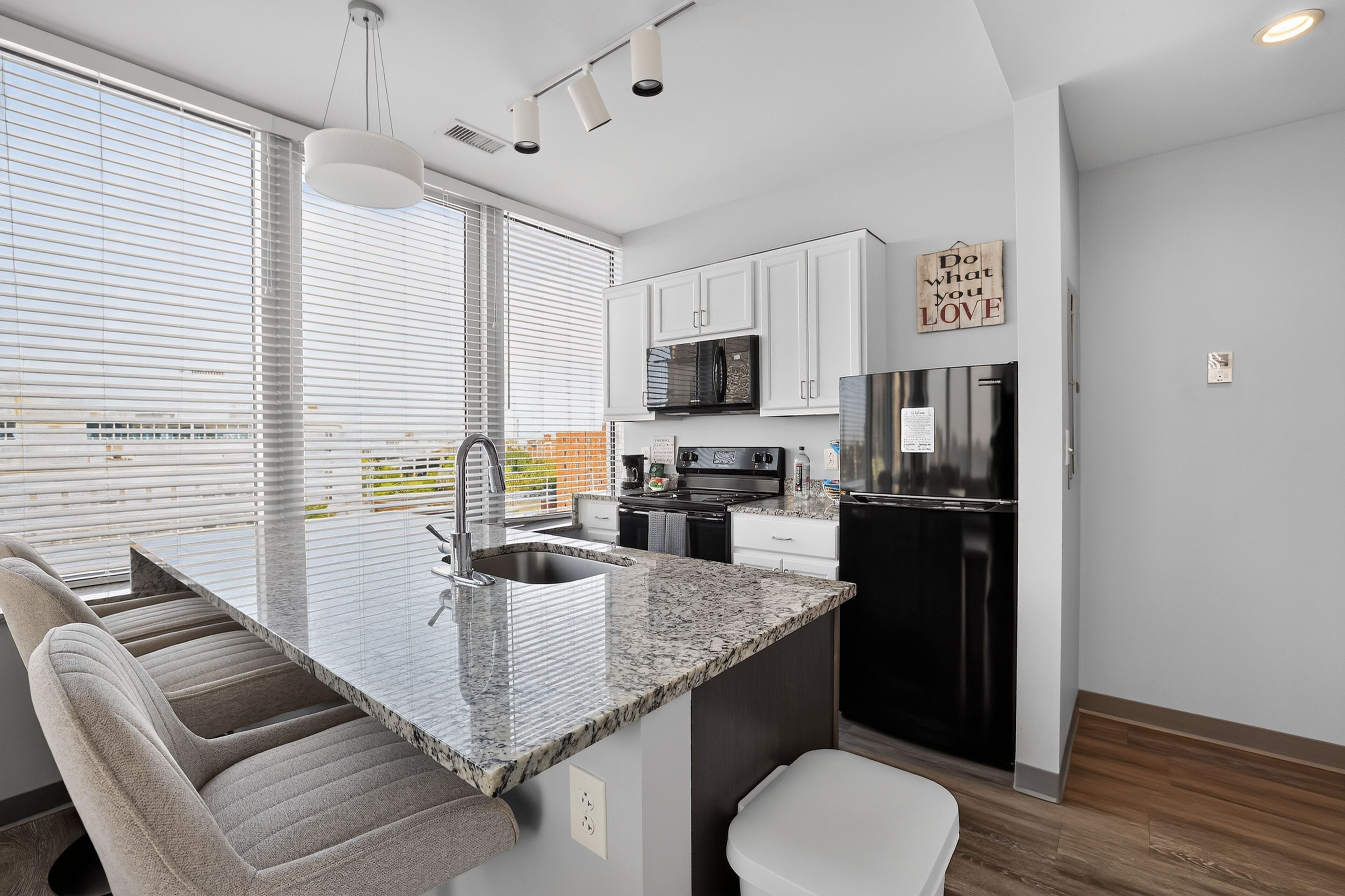 A modern kitchen with a central island, stainless steel appliances, and a view through large windows.
