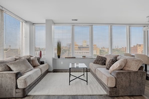 A modern living room with two sofas, a coffee table, and large windows with blinds. - Downtown Condo | Walk to Playhouse Square (Cleveland)
