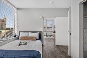A modern bedroom with a bed, bedside table, and a view of the city through large windows. - Downtown Condo | Walk to Playhouse Square (Cleveland)