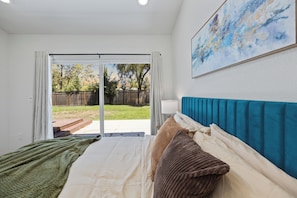 A bedroom with a bed, a nightstand, a lamp, a painting on the wall, and a view through a sliding glass door to the outside. - 4BD 3BA Modern Home with Backyard. Near SF, Concord, Oakland & Napa Winery (Concord)