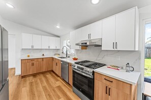 A modern kitchen with white cabinets, a stainless steel stove, and a wooden countertop.