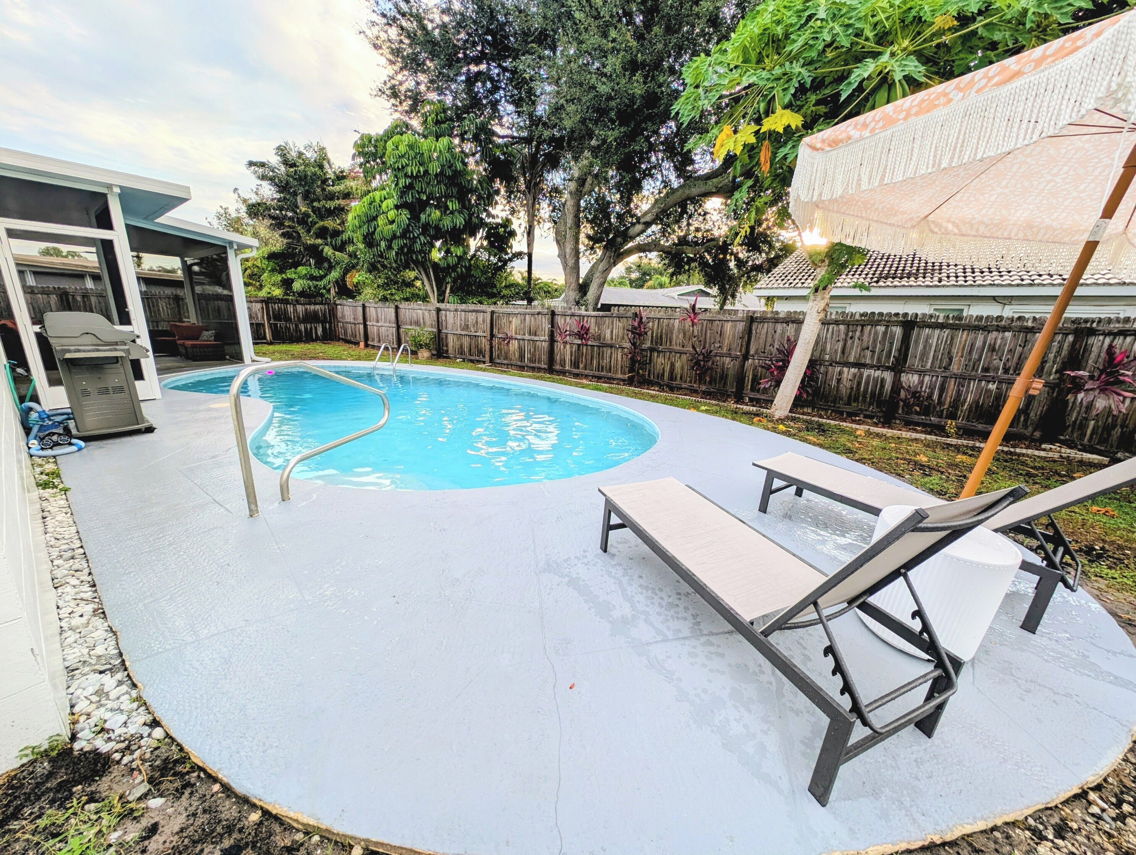 A backyard with a swimming pool, lounge chairs, and a wooden fence.
