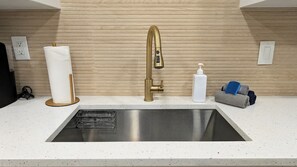 A modern kitchen with a stainless steel sink, a gold faucet, a paper towel dispenser, a soap dispenser, and a towel holder. - A Haven of Sun and Fun in Largo; A Private Oasis in the heart of everything (Largo)