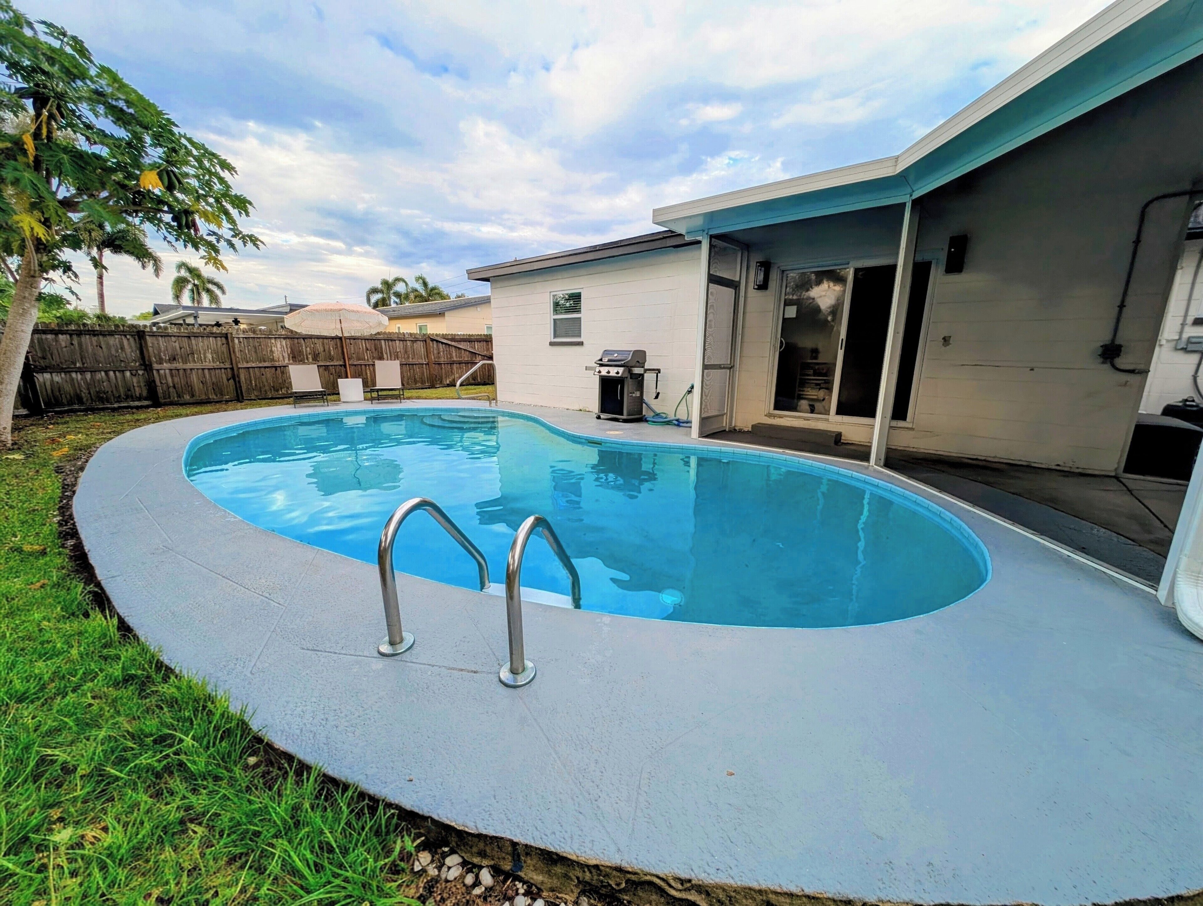 Una piscina con escalera incorporada, rodeada de césped y una valla de madera.