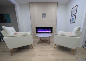 A modern living room with two white sofas, a round table, and a flat-screen TV displaying a fireplace. - A Haven of Sun and Fun in Largo; A Private Oasis in the heart of everything (Largo)